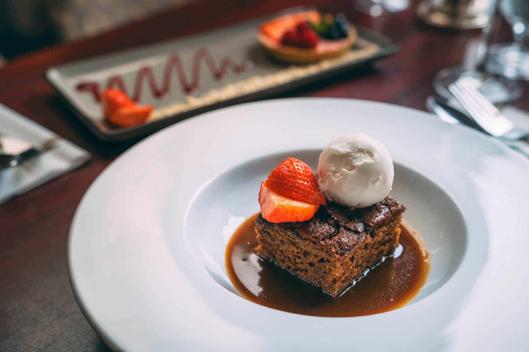 A dessert plate with a chocolate cake, a strawberry, and a scoop of ice cream.