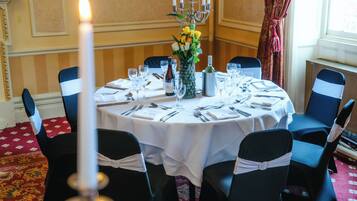 A round dining table set with chairs, a vase with flowers, a candle, and a bottle of wine.