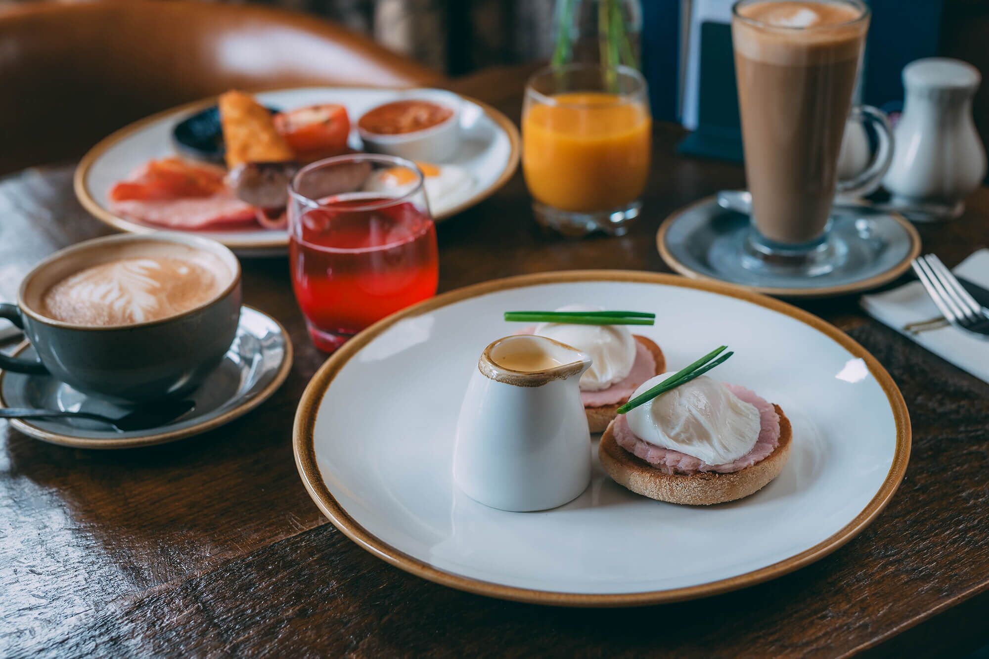 Desayuno con huevos Benedict, café, jugo de naranja y croissants sobre una mesa de madera.