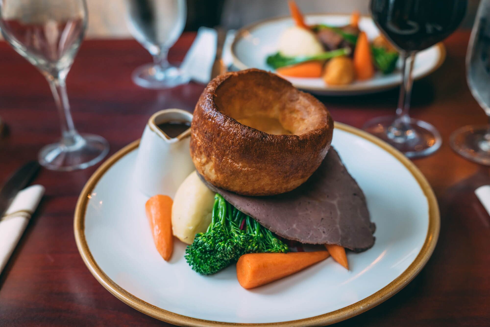A plate with a Yorkshire pudding, mashed potatoes, carrots, and broccoli.
