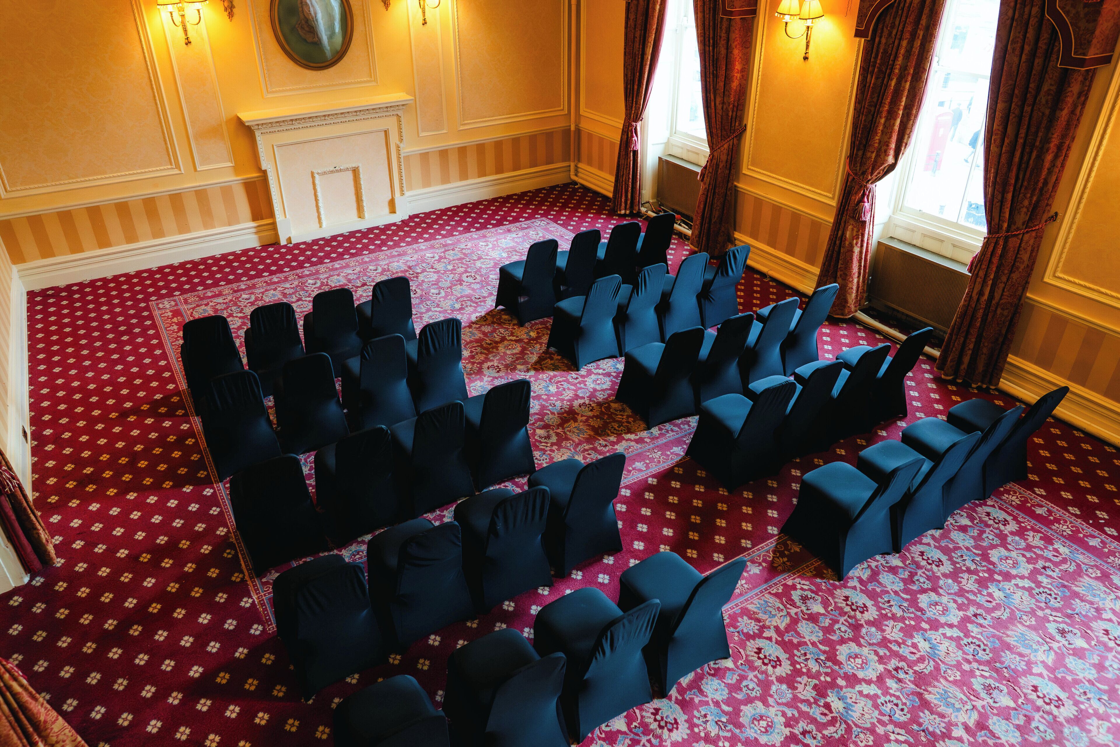 Une salle de conférence avec des rangées de chaises, une moquette à motifs et une cheminée.
