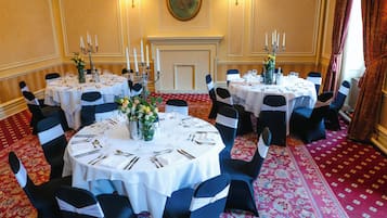 Un comedor formal con mesas redondas, sillas negras adornadas con cintas blancas y una alfombra roja estampada.