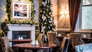 Une pièce chaleureuse avec une cheminée, un sapin de Noël et un tableau encadré au-dessus. On y trouve deux tables et quatre chaises.