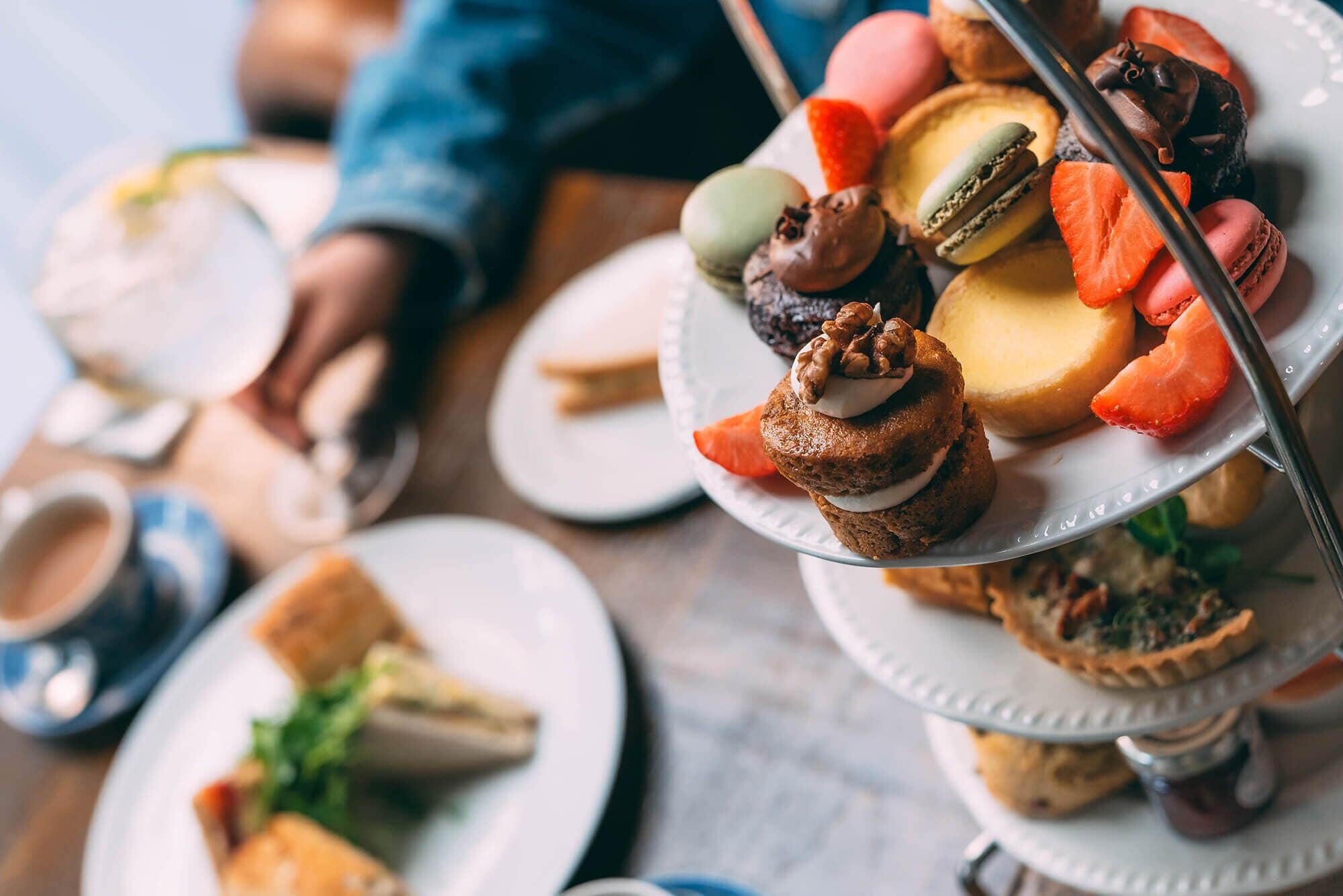A variety of desserts on a multi-tiered stand, including macarons, pastries, and a slice of cake, with a cup of coffee in the background.