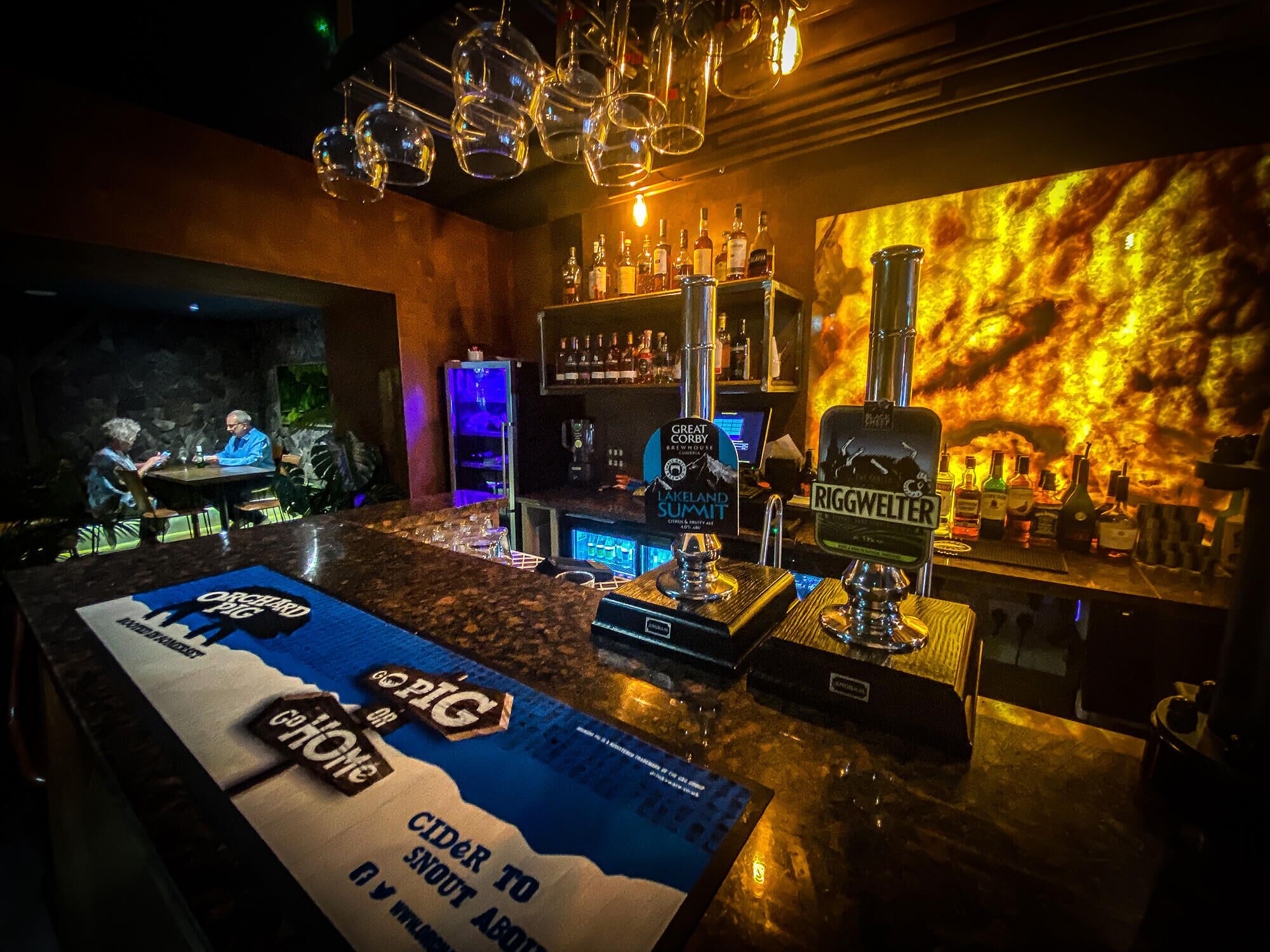 Een bar met een toonbank, diverse flessen en een bord waarop staat 