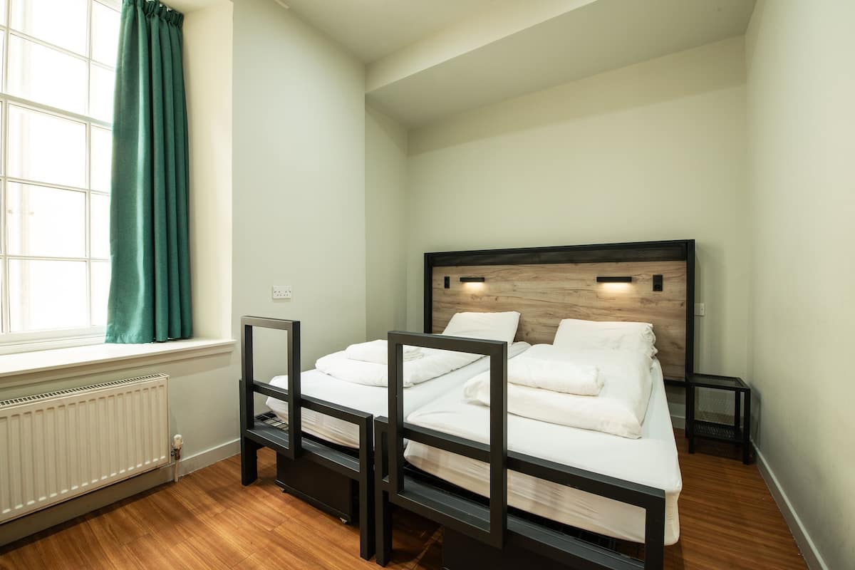 A bedroom with a wooden headboard, white bedding, a window with curtains, and a radiator.