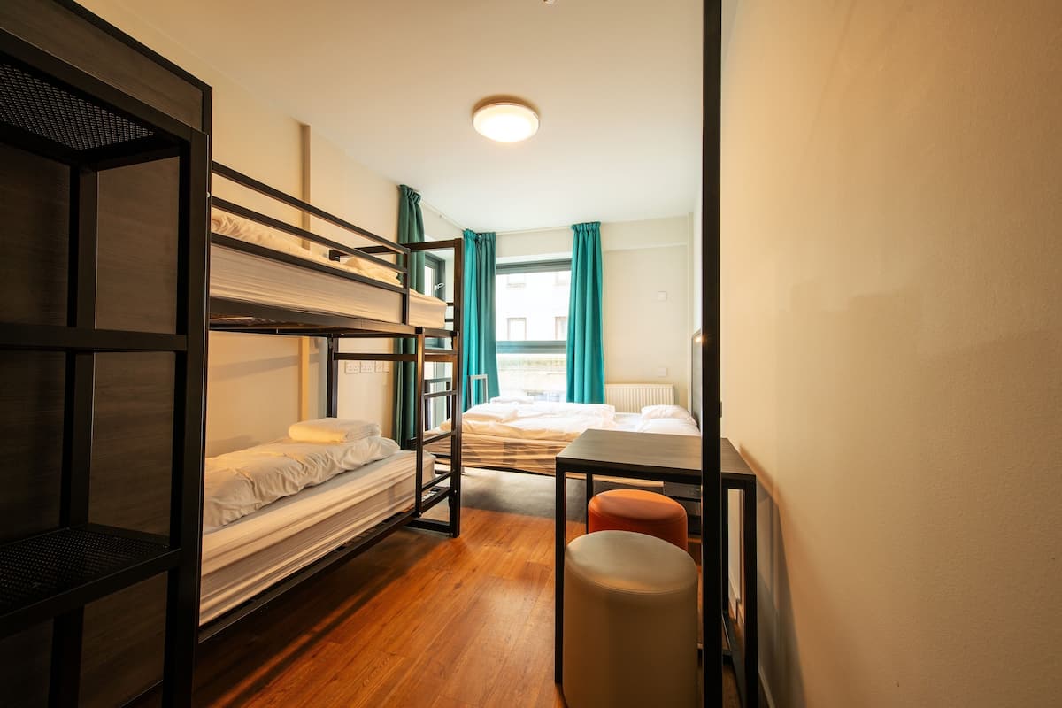 A dormitory room with bunk beds, a desk, and a window with curtains.