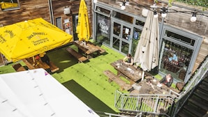 An outdoor patio area with wooden tables and benches, yellow umbrellas, and a view of the interior through a glass wall. - a&o Edinburgh City - Hostel (Edinburgh)