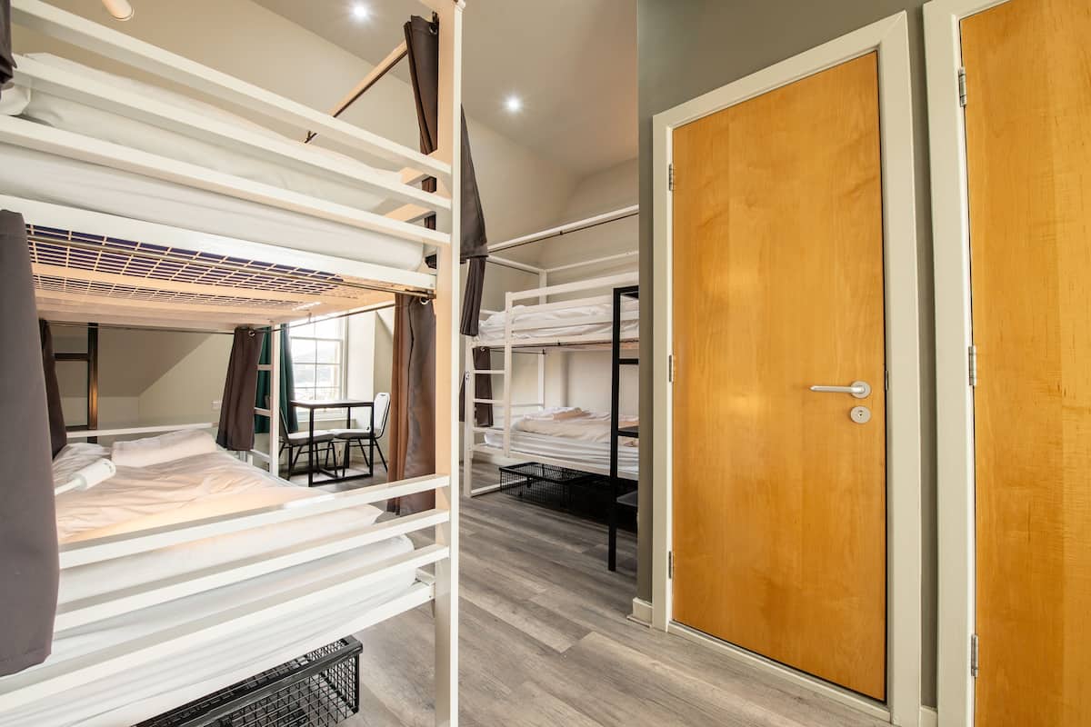 A dormitory room with bunk beds, a wooden door, and a small table with chairs.