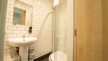 Un baño con pared de azulejos blancos, un lavamanos blanco y una ducha con mampara de vidrio.