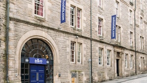 A historic stone building with a blue door labeled 'a&o' and banners for 'aohostels.com'. - a&o Edinburgh City - Hostel (Edinburgh)