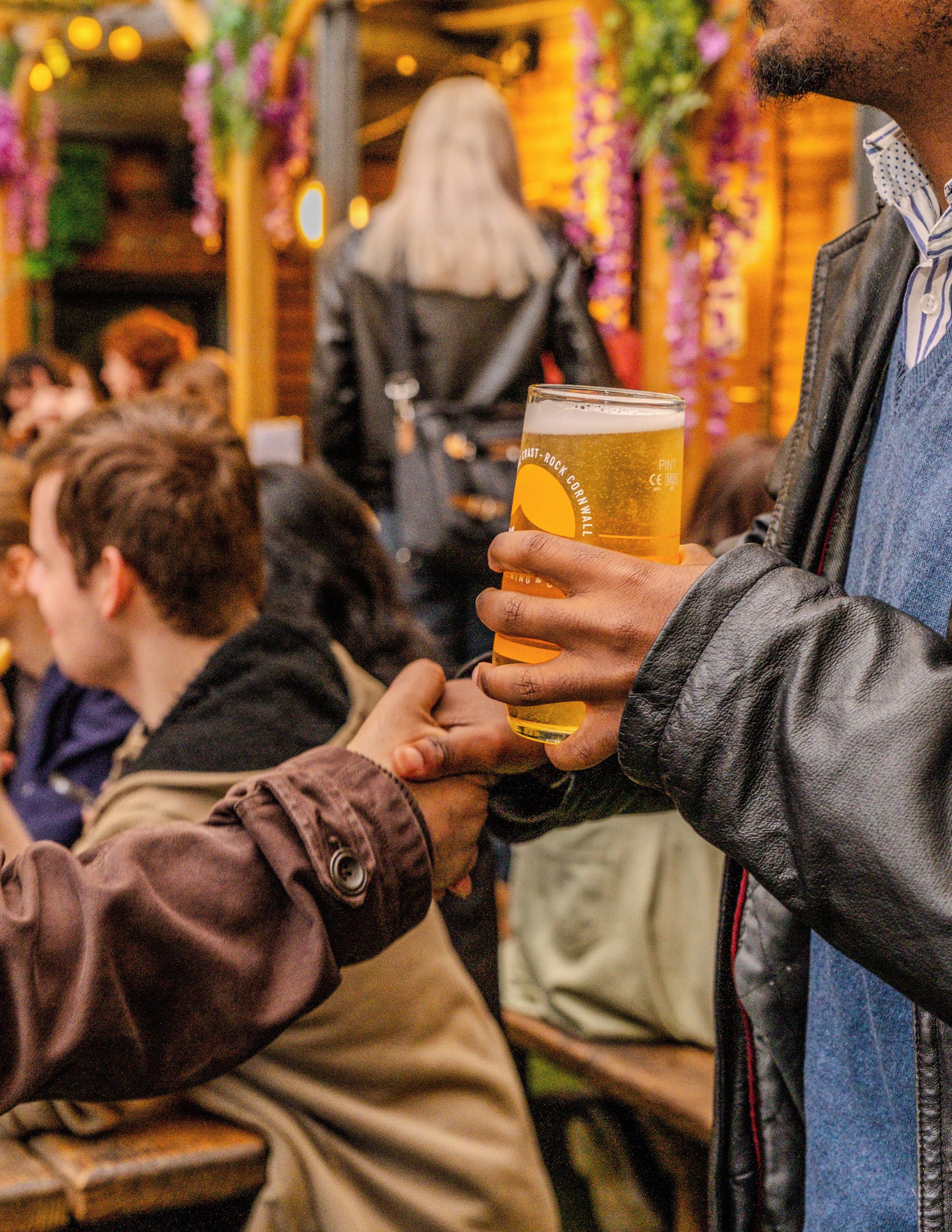 A person holding a glass of beer, with another person reaching out to take it.