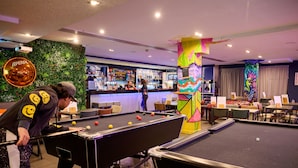 A pool table in a room with a bar area and a green wall with a projector. - a&o Edinburgh City - Hostel (Edinburgh)