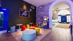 A modern lobby with a blue door, round seating, a Zuronet ATM, and a stone wall. - a&o Edinburgh City - Hostel (Edinburgh)