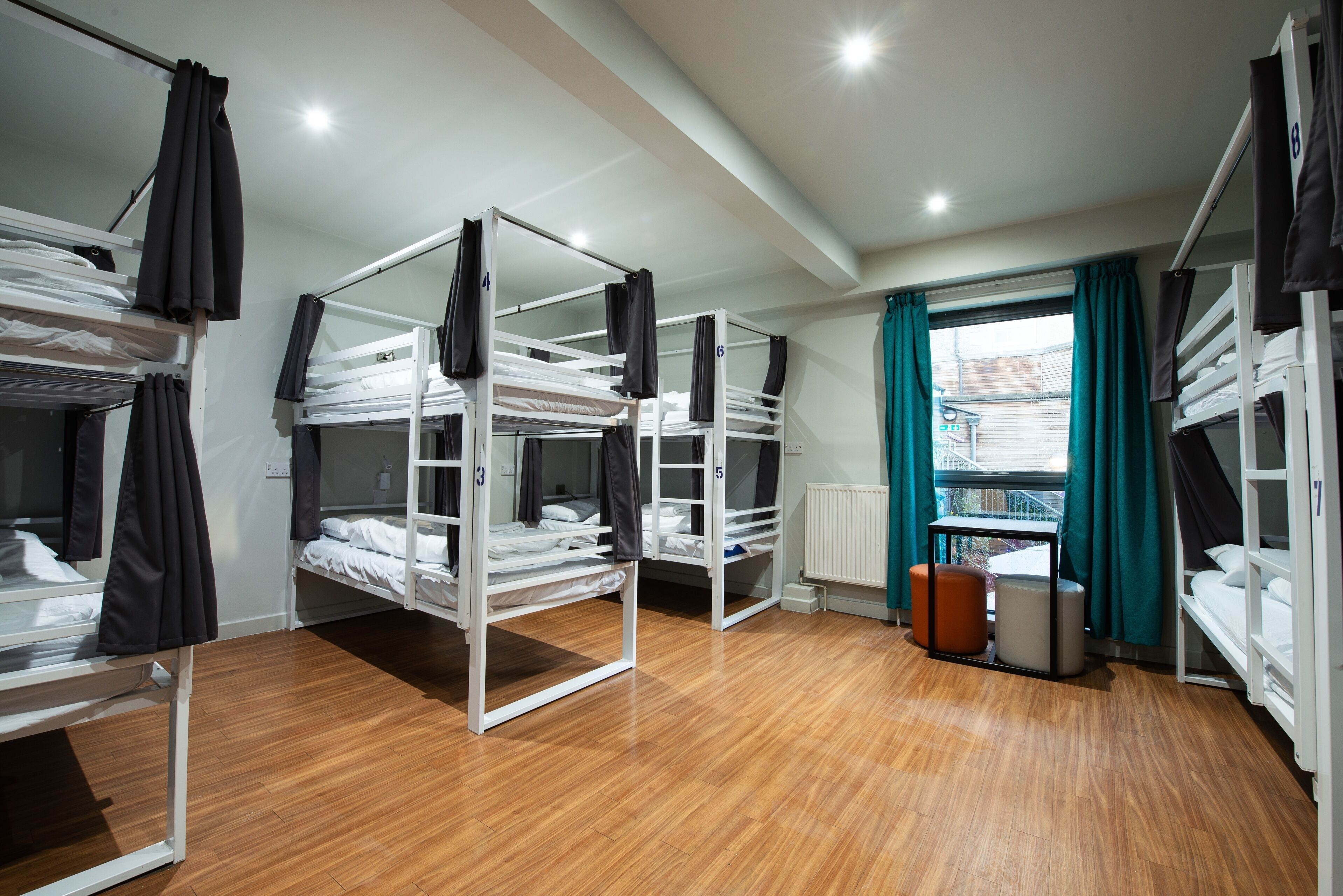A dormitory room with bunk beds, a window with curtains, and a radiator.
