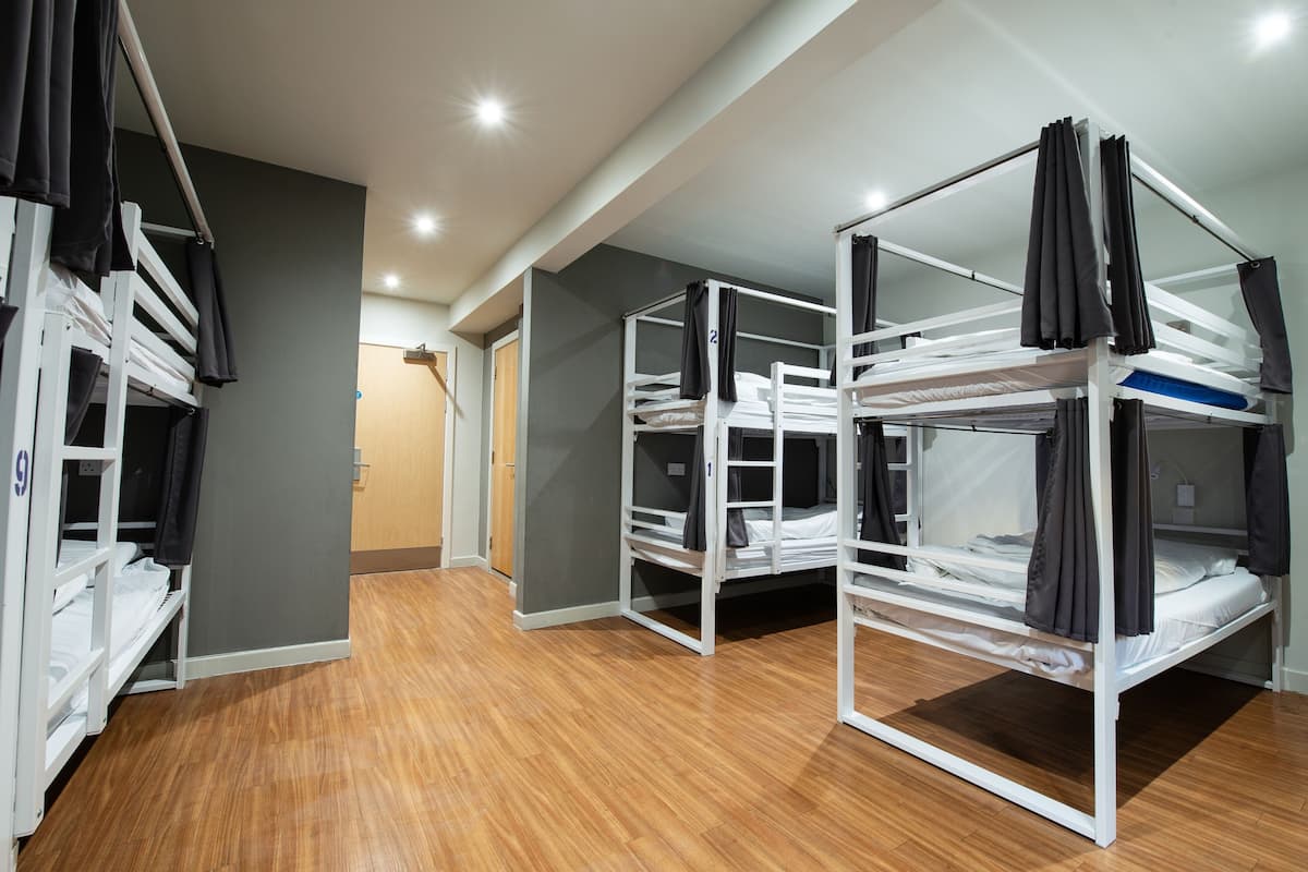 A dormitory room with bunk beds, wooden flooring, and a door leading to another room.
