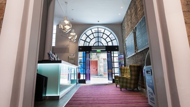 A hotel lobby with a wooden floor, a red carpet, and a reception desk. - a&o Edinburgh City - Hostel (Edinburgh)