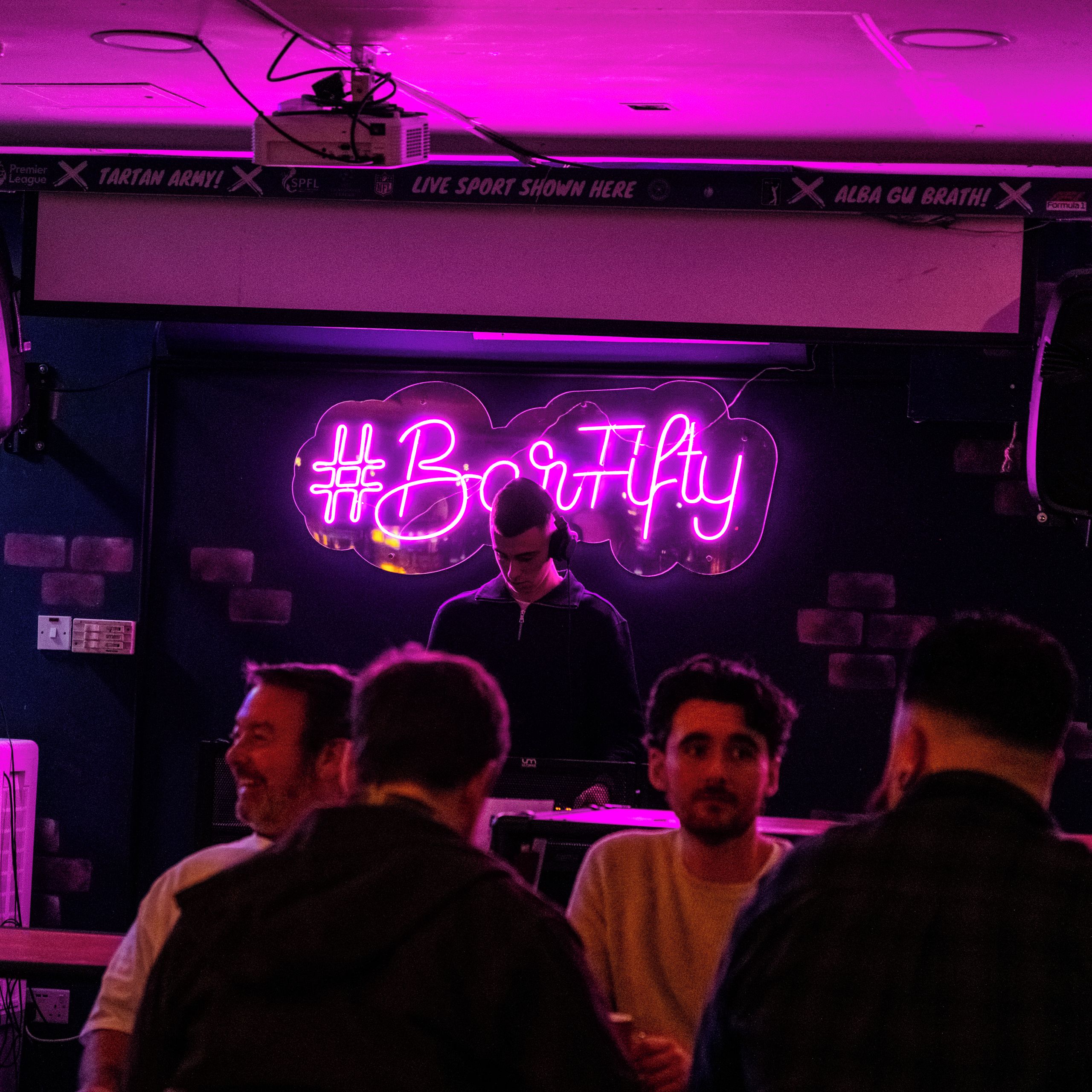 Una habitació amb un cartell de neó que diu '#BobbyFlyy' i una persona dret davant.