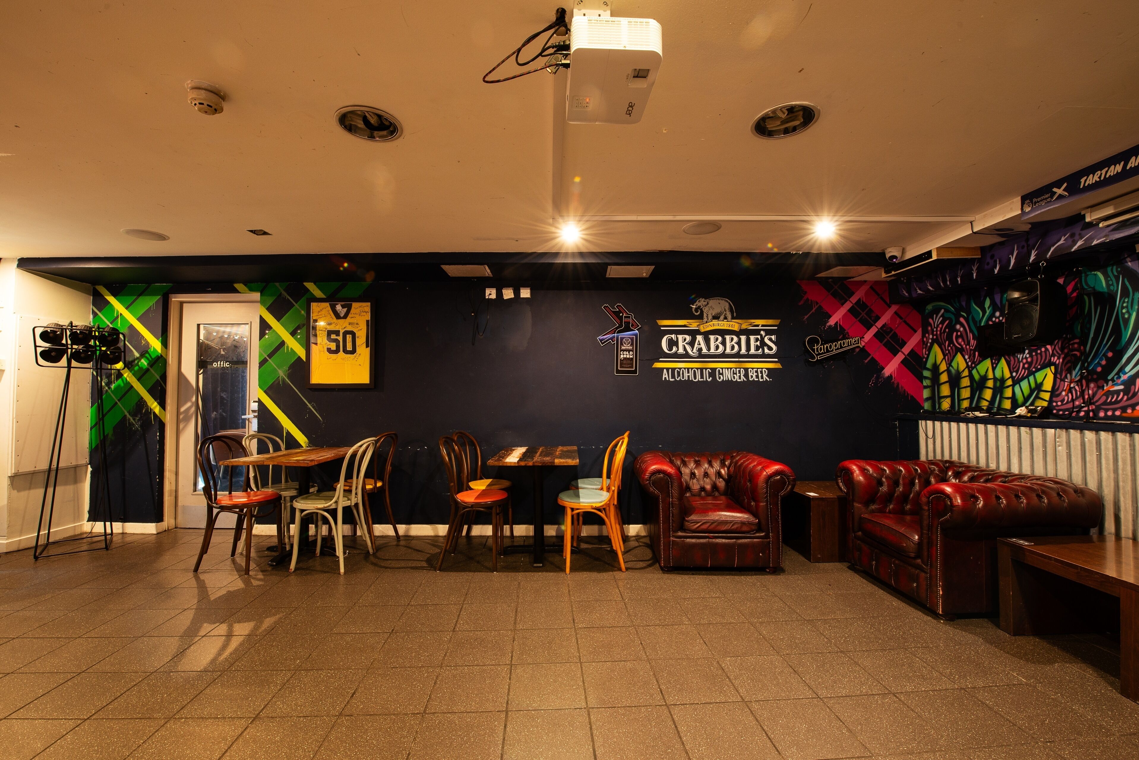 A bar area with a counter, stools, and a couch. There are signs on the wall, including one that says "CRABBIE'S ALCOHOLIC GINGER BEER."