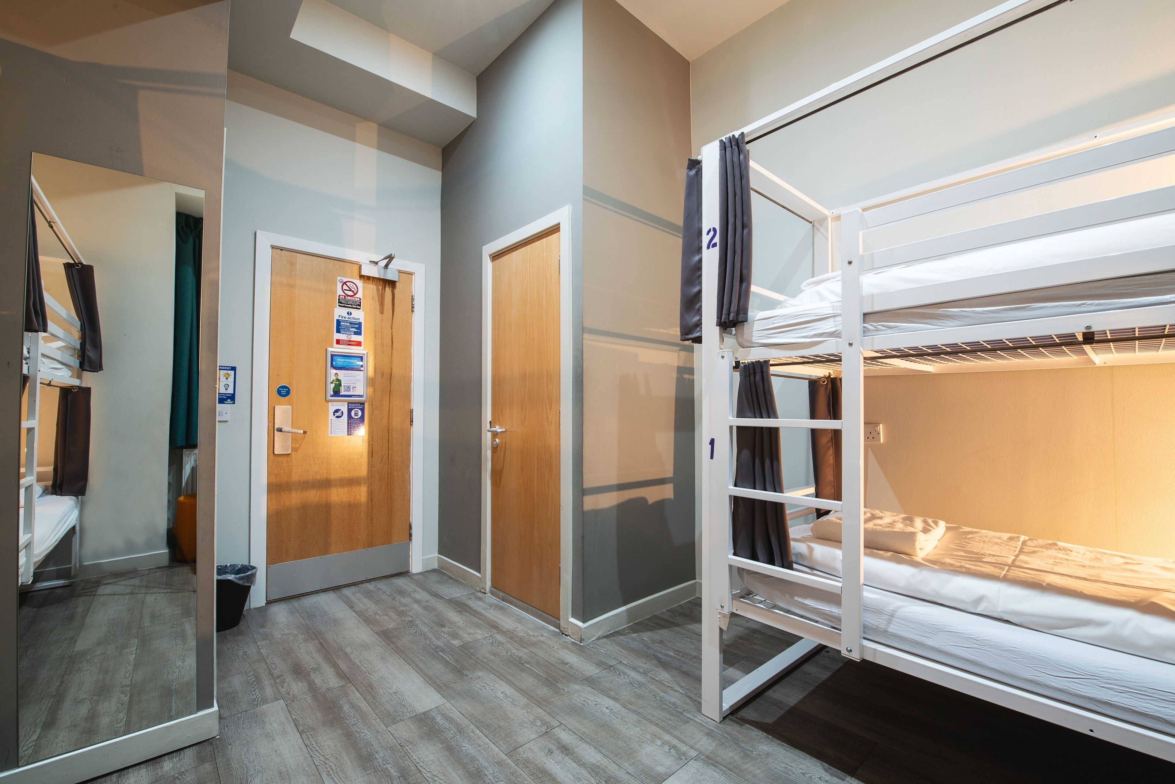 A hotel room with a bunk bed, a wooden door, a mirror, and a small seating area.