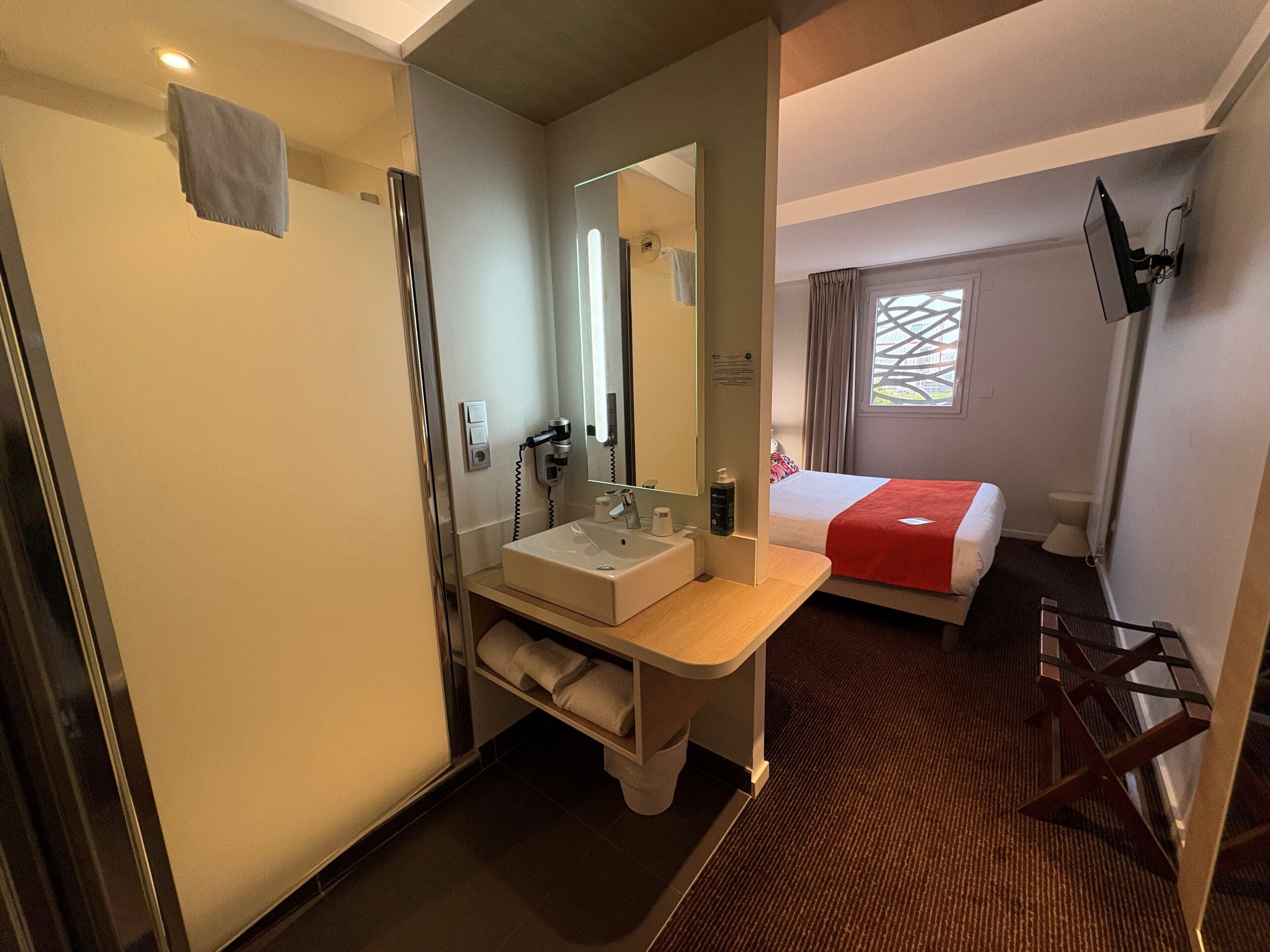 Ein Hotelzimmer mit Bad, Bett, Fernseher und Fenster.