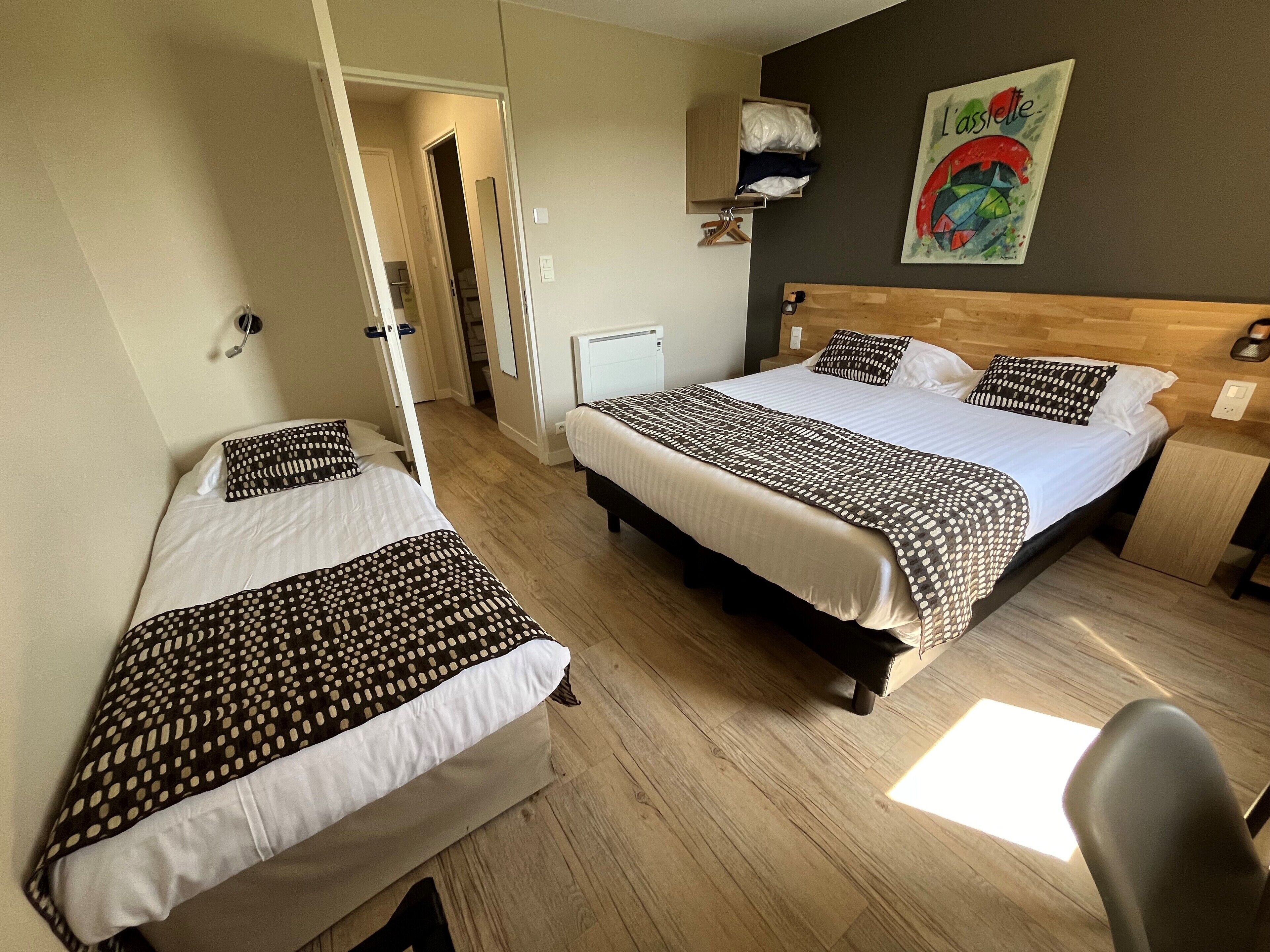 Ett hotellrum med två sängar, en sänggavel i trä, en tavla på väggen och ett litet nattduksbord.