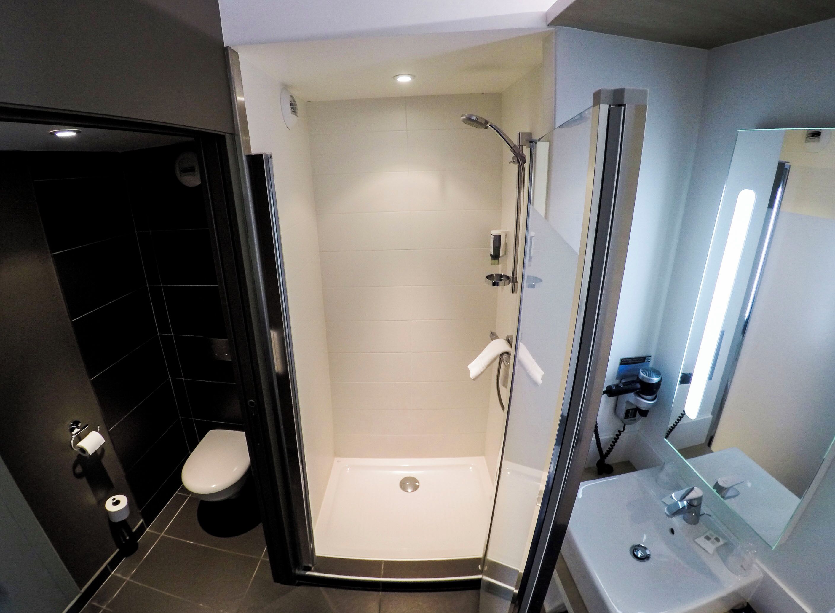 Un baño moderno con ducha envuelta en vidrio, inodoro y lavabo con espejo.