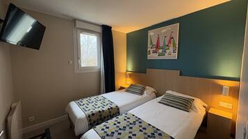Habitación de hotel con dos camas, un televisor montado en la pared, una ventana con cortinas y un cuadro de veleros.