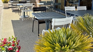 Un patio al aire libre con mesas y sillas, un muro de ladrillo y vistas al campo.
