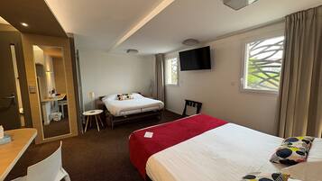 A hotel room with a bed, a desk, a chair, a TV, and a window with curtains.