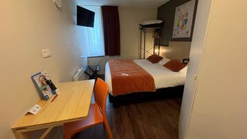 Een hotelkamer met een bed, een bureau met stoel, een raam met gordijnen, een nachtkastje en een aan de muur bevestigde televisie.