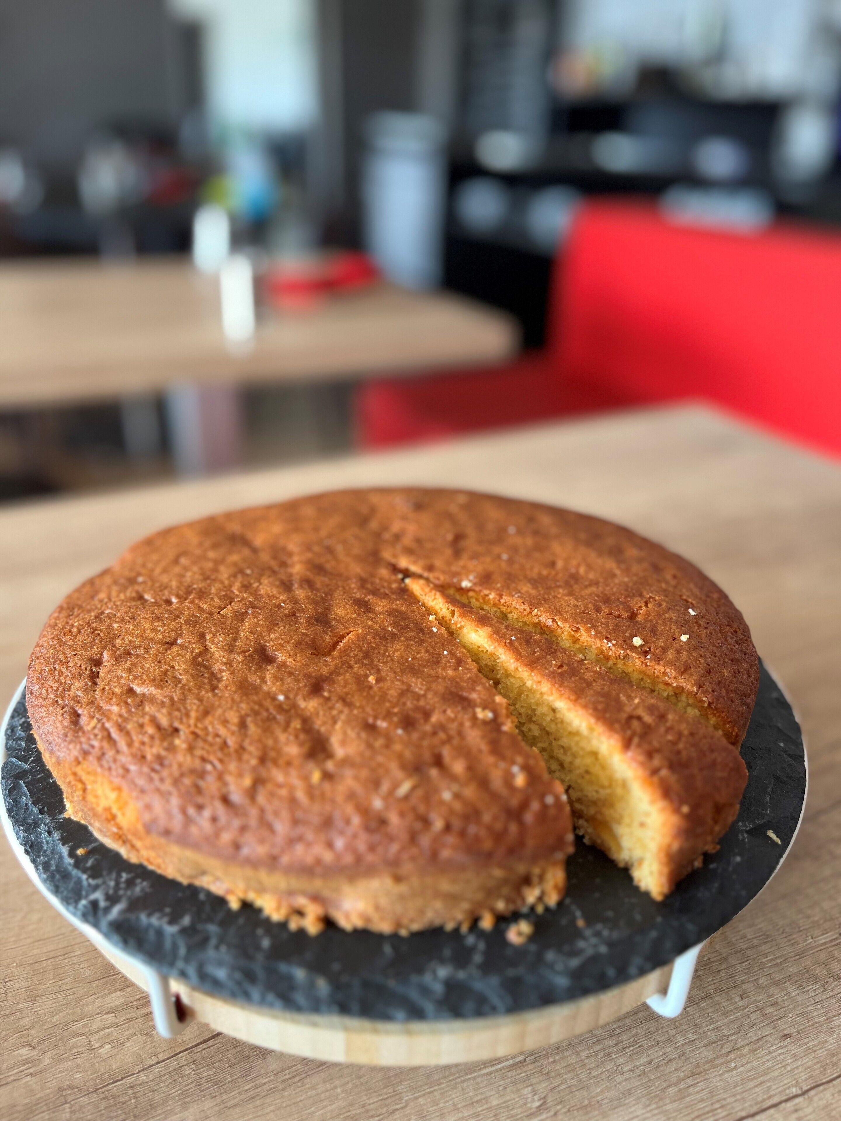 Un pastel redondo con una porción cortada, sobre un plato de pizarra negra sobre una mesa de madera.