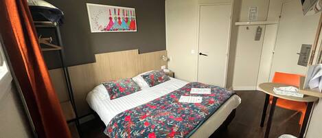 Habitación de hotel con cama, escritorio, silla, armario y un cuadro en la pared.