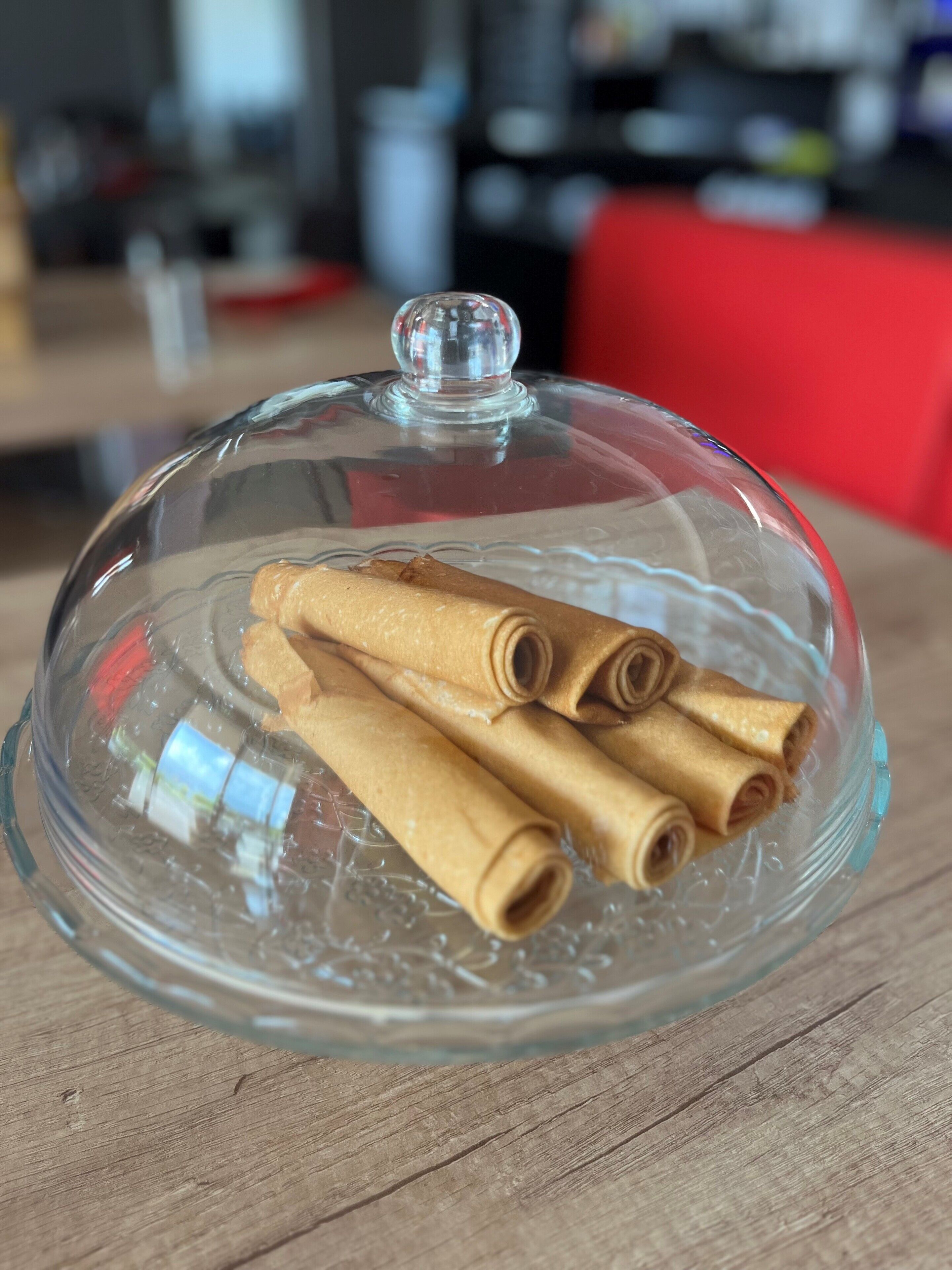 Eine gläserne Kuppel bedeckt ein Serviergefäß mit gefüllten Teigtaschen auf einem Holztisch.