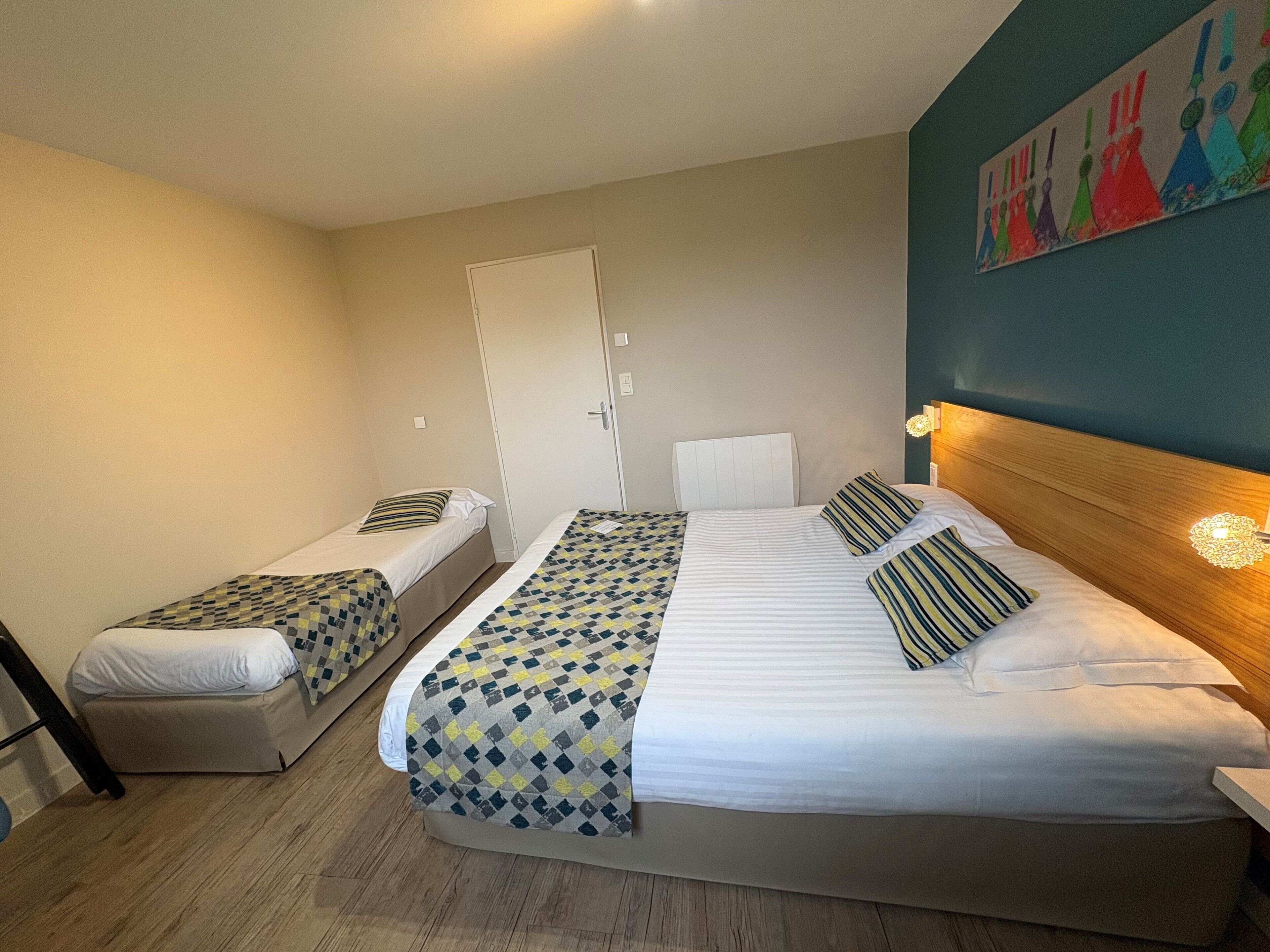 A hotel room with two single beds, a wooden headboard, a door, and a colorful abstract painting on the wall.