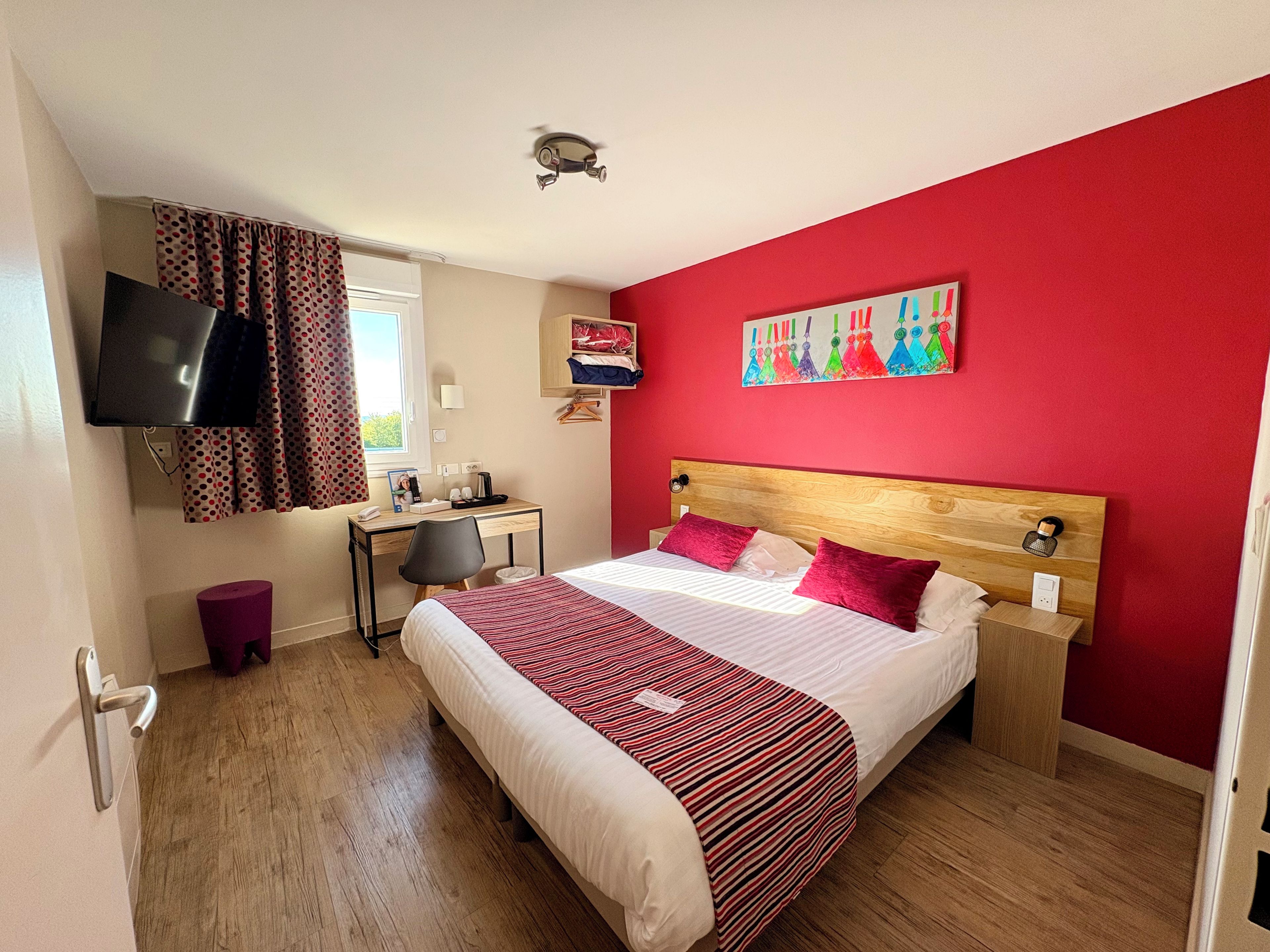A hotel room with a bed, desk, chair, and a television.