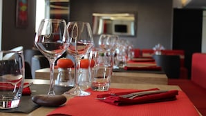 Mesa para comer dispuesta con copas de vino, vasos de agua y un mantel individual rojo.