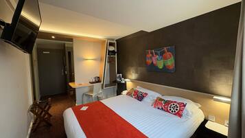 A hotel room with a bed, a desk, a chair, a TV, and a painting on the wall.