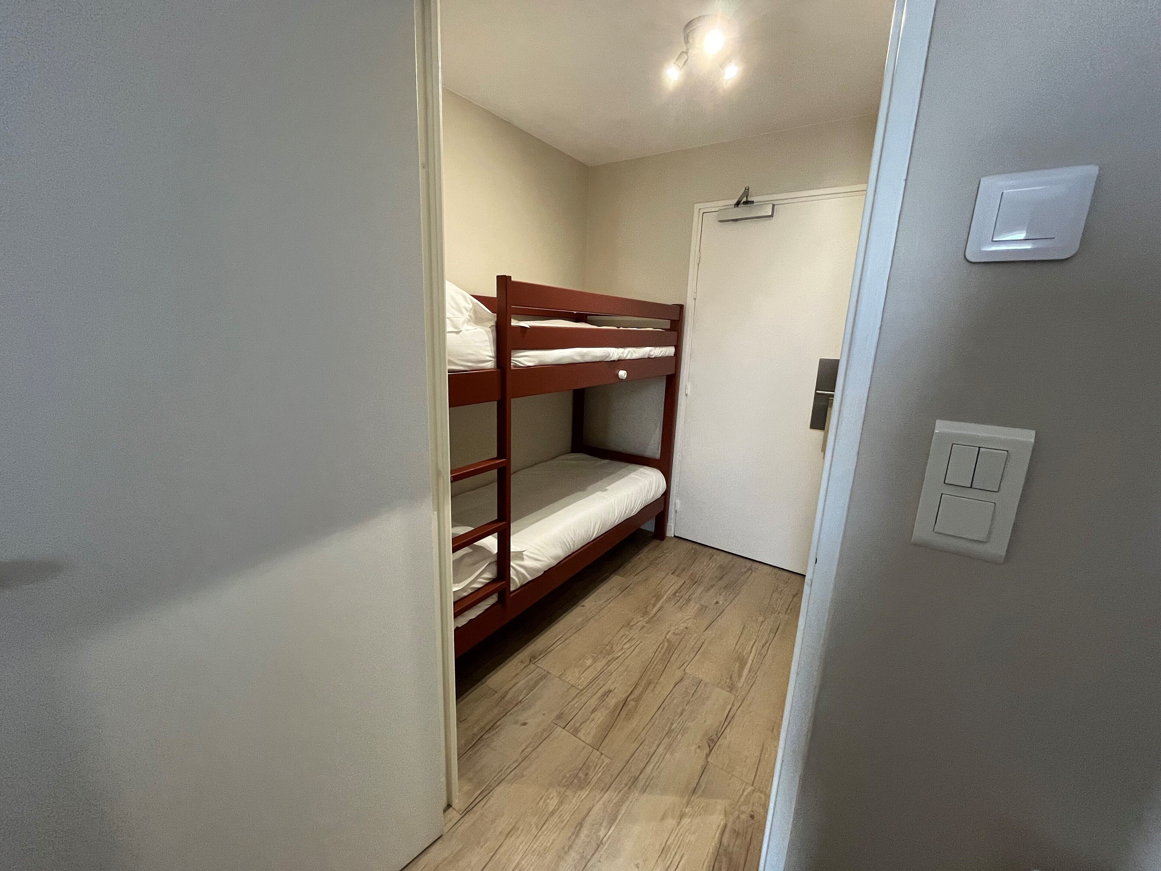 A small, narrow room with a wooden bunk bed and a door.