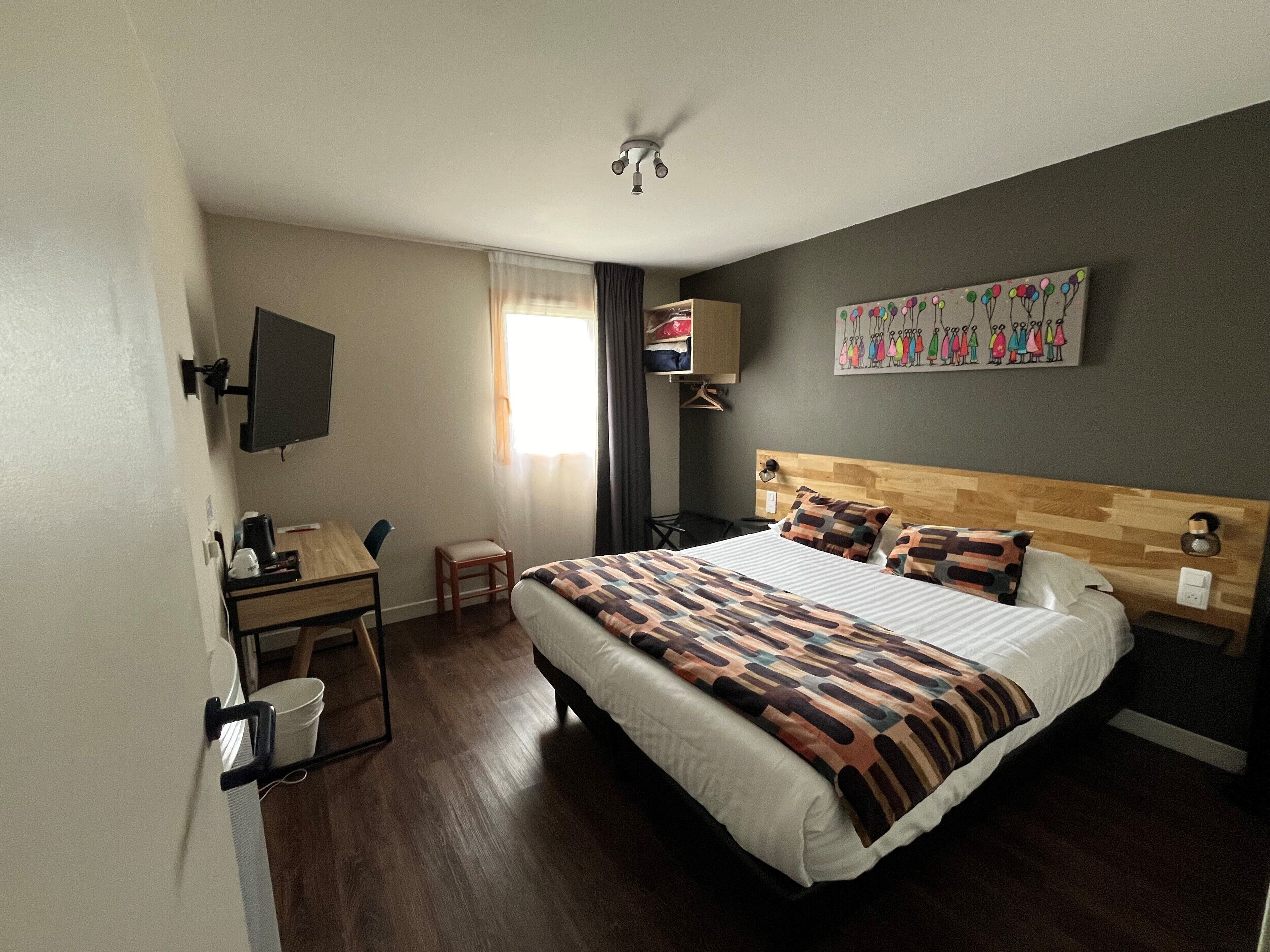 Una habitación de hotel con cama, escritorio, silla, televisor y un cuadro en la pared.