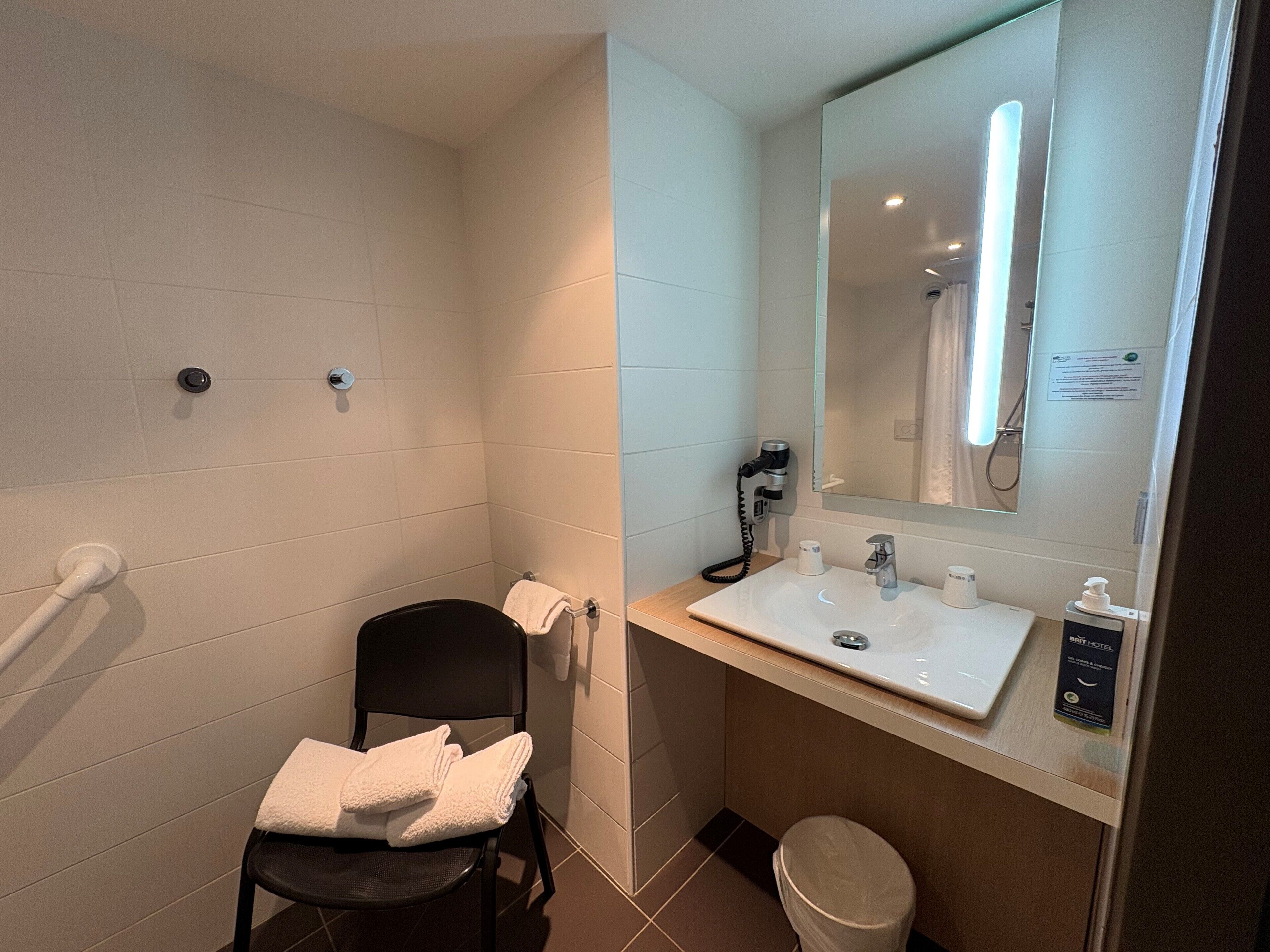 Baño con ducha, inodoro, lavamanos y silla con toallas.