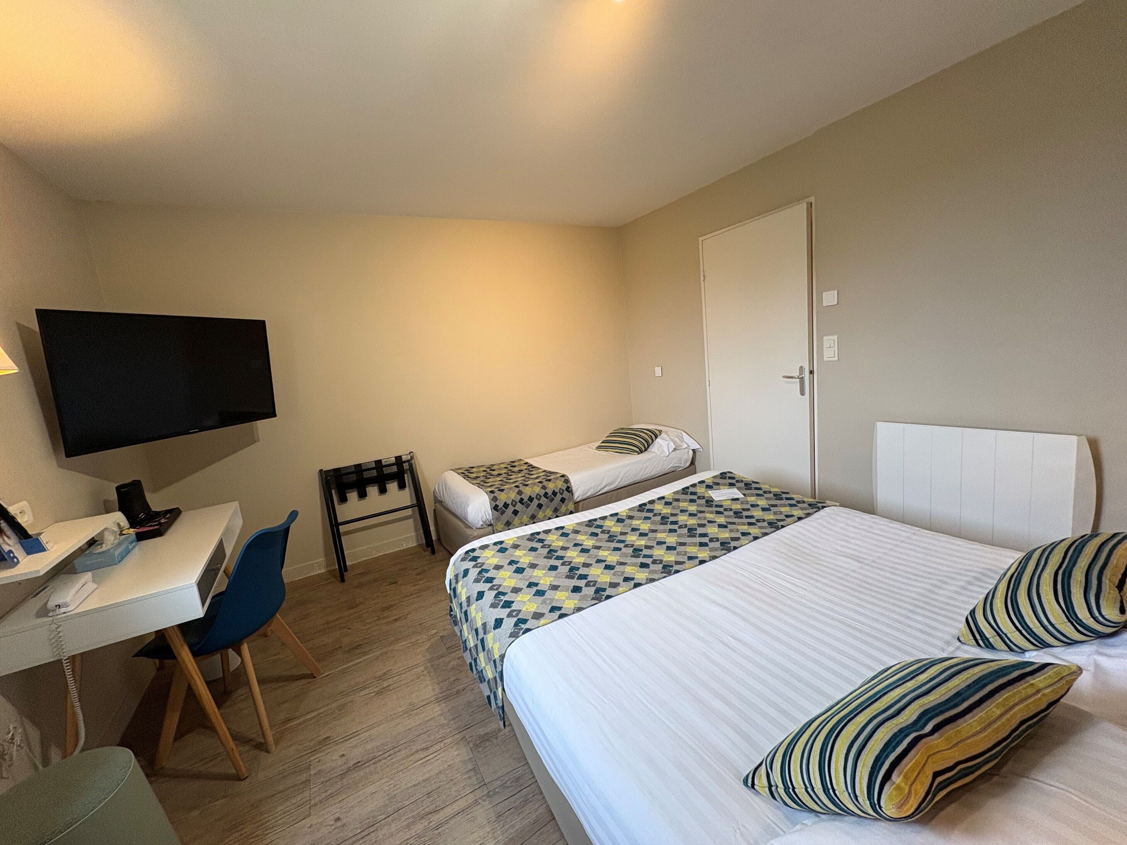 A hotel room with a bed, a desk with a chair, a television, and a door.