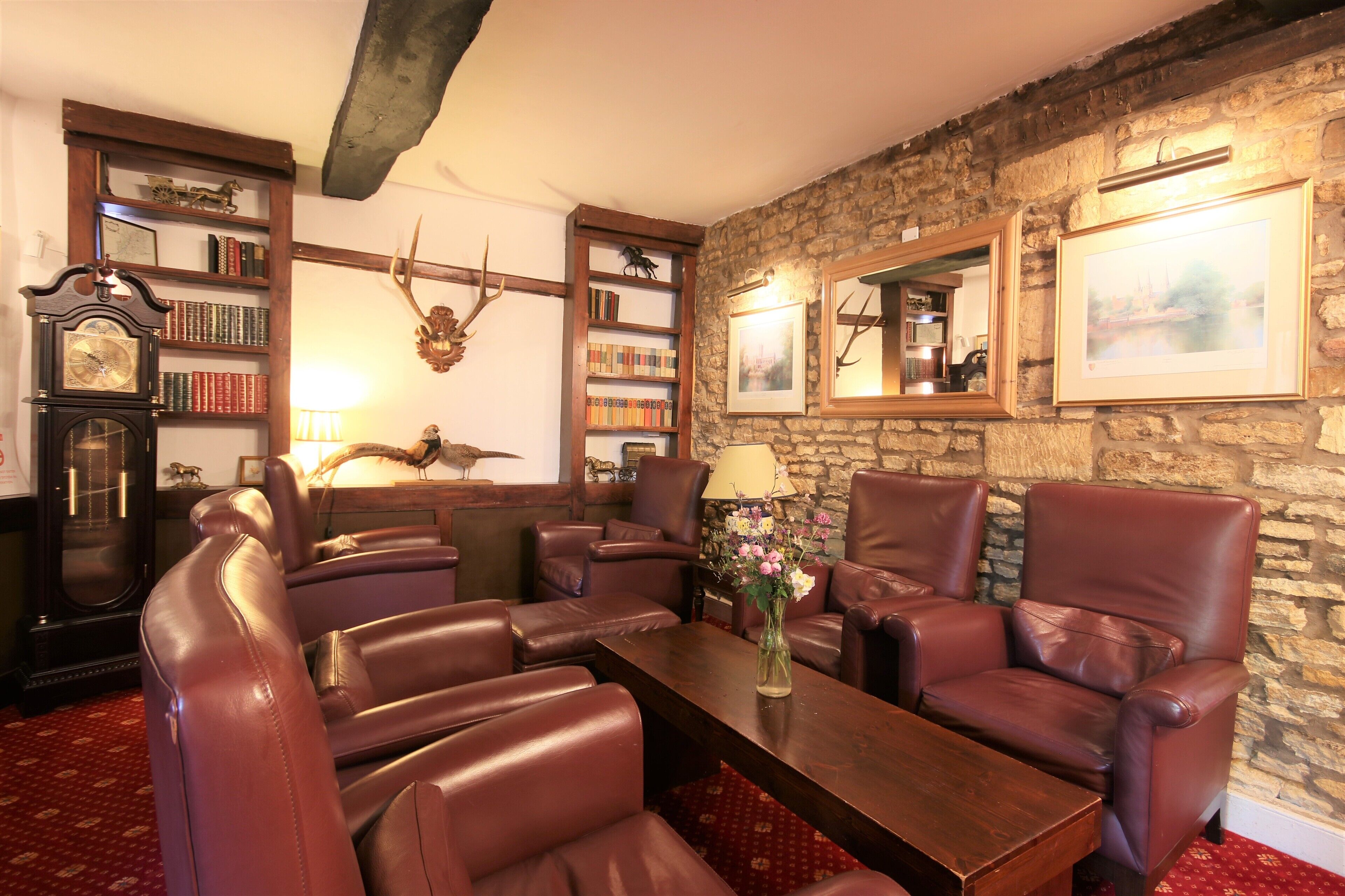 A room with leather chairs, a wooden coffee table, bookshelves, a clock, and a stone wall.