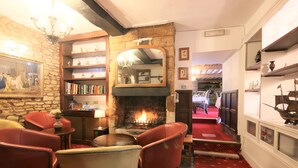 A cozy room with a fireplace, leather chairs, a bookshelf, and a stone wall. - The Crown Hotel (Moreton-in-Marsh)
