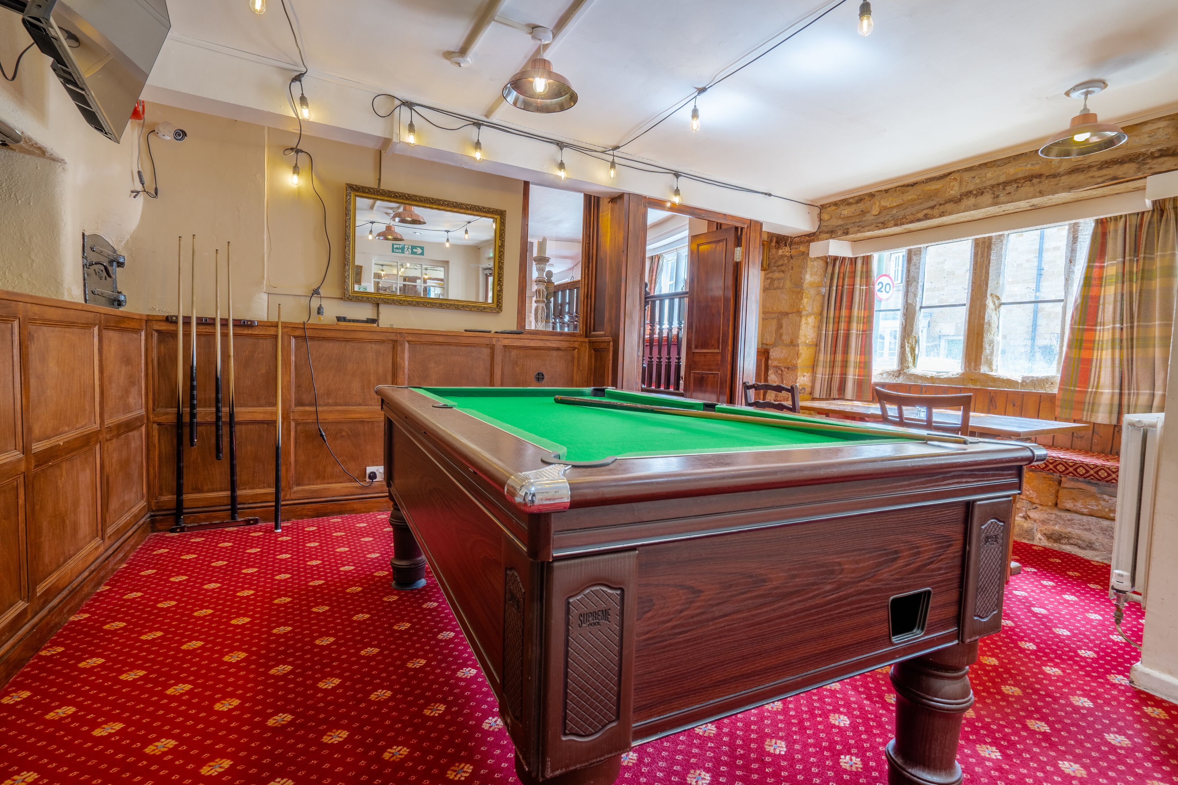 A pool table in a room with wooden paneling, a red patterned carpet, and a mirror on the wall.