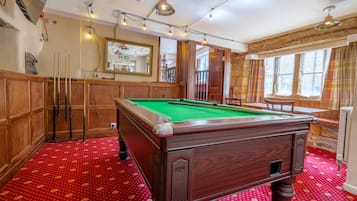 A pool table in a room with wooden paneling, a red patterned carpet, and a mirror on the wall.
