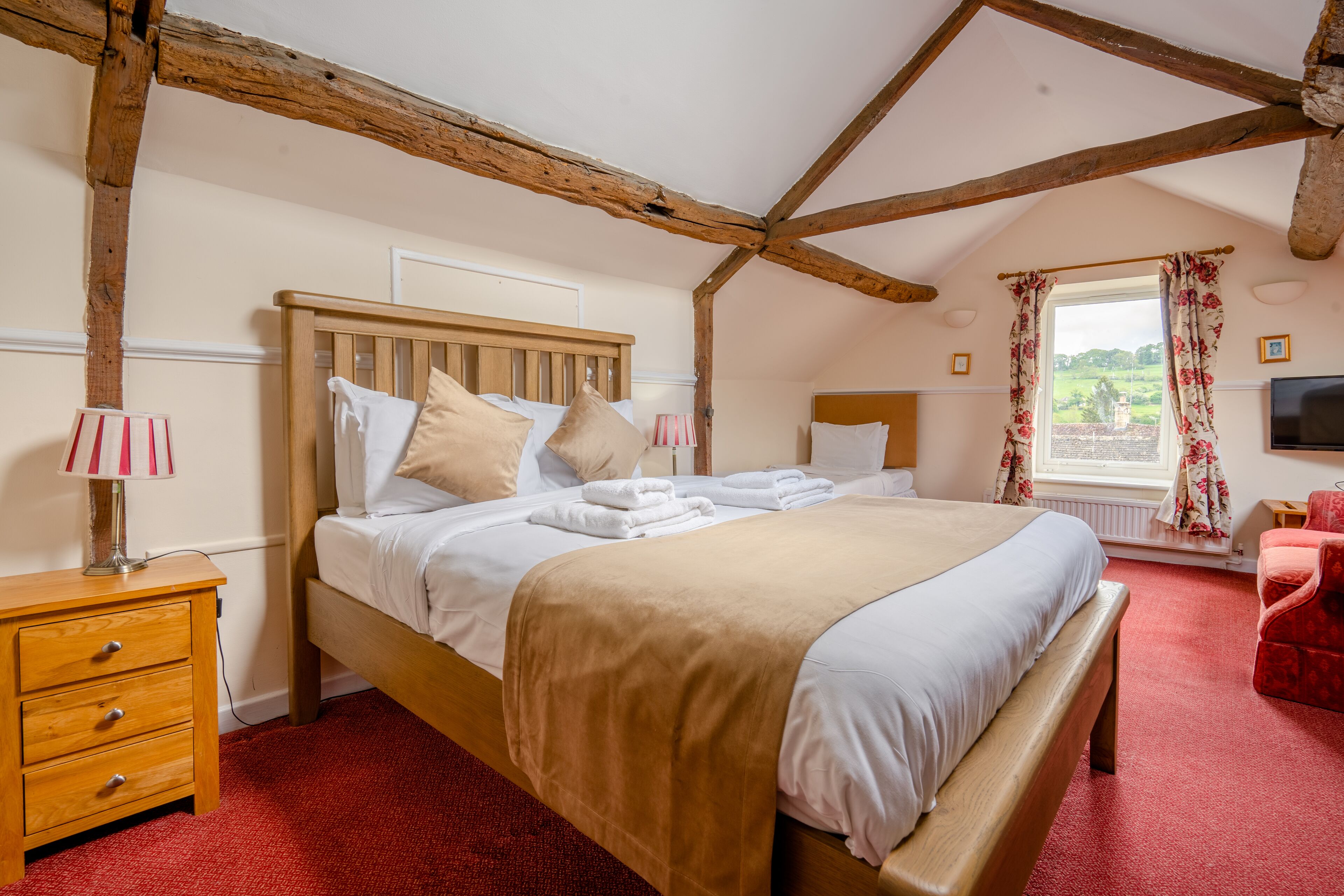 Une chambre à coucher avec un lit en bois, une table de chevet, une moquette rouge, une fenêtre avec des rideaux et un fauteuil rouge.