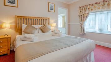 A neatly made bed with a wooden headboard, two bedside lamps, and a red carpeted floor.