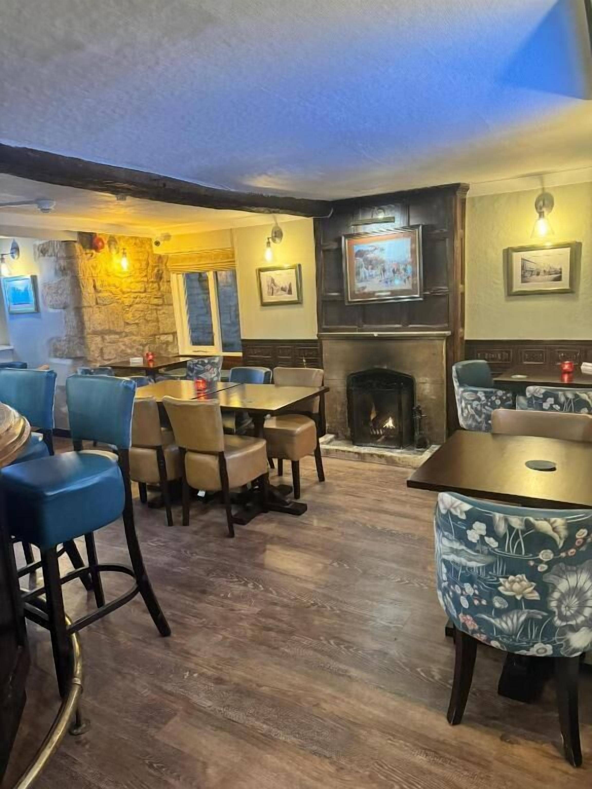 Een restaurant met houten vloeren, blauwe en beige stoelen en een open haard.