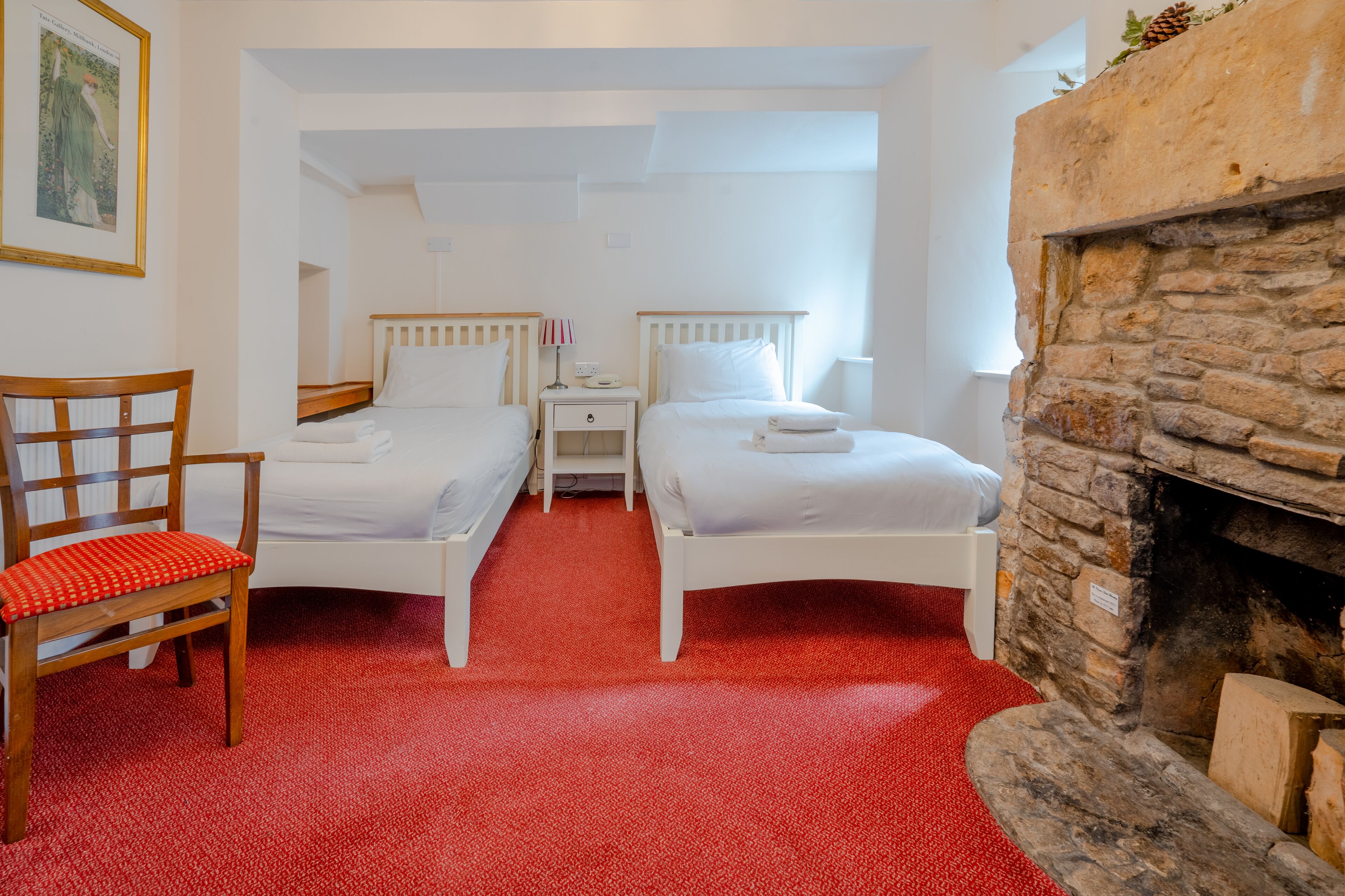 Una habitación con dos camas individuales, una silla de madera, una chimenea de piedra y una alfombra roja.